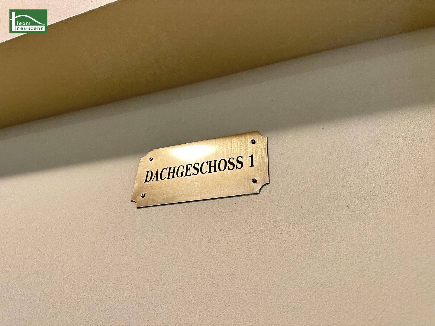 Messingschild an einer Wand, das den Zugang zum ersten Dachgeschoss anzeigt.