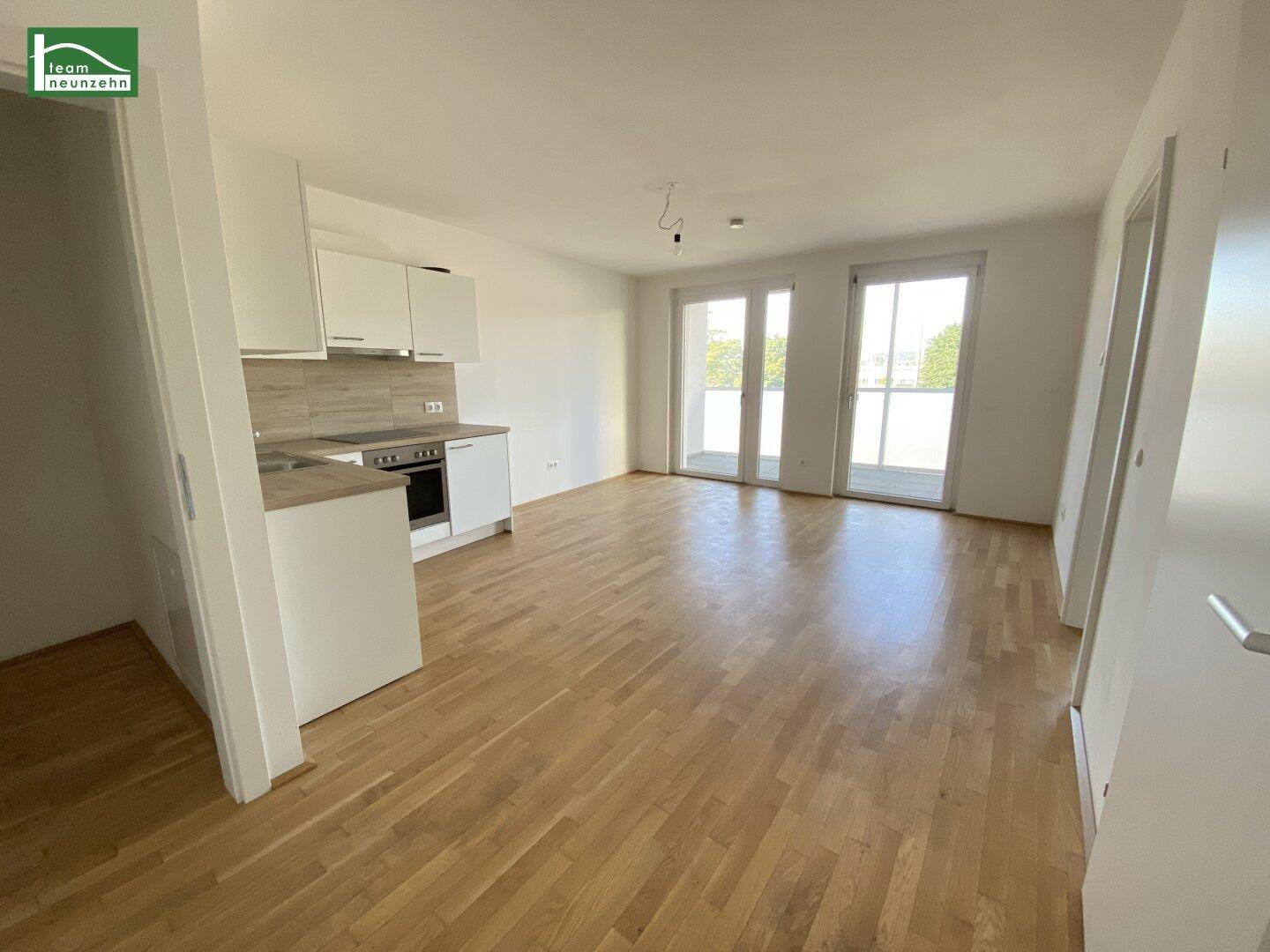 Heller offener Wohn-Essbereich mit integrierter Küche, Parkettboden und Zugang zum Balkon.
