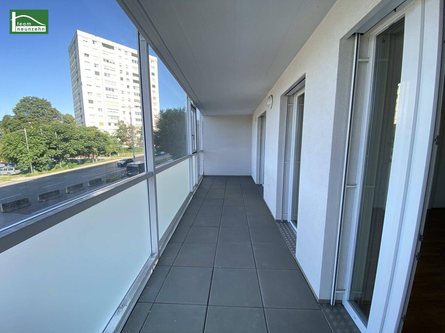 Langer Balkon mit Glasbrüstung und Blick auf die Stadt und ein Hochhaus in der Ferne.
