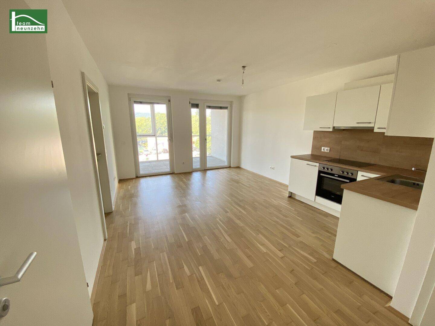 Heller offener Wohn-Essbereich mit integrierter Küche, Parkettboden und Zugang zum Balkon.