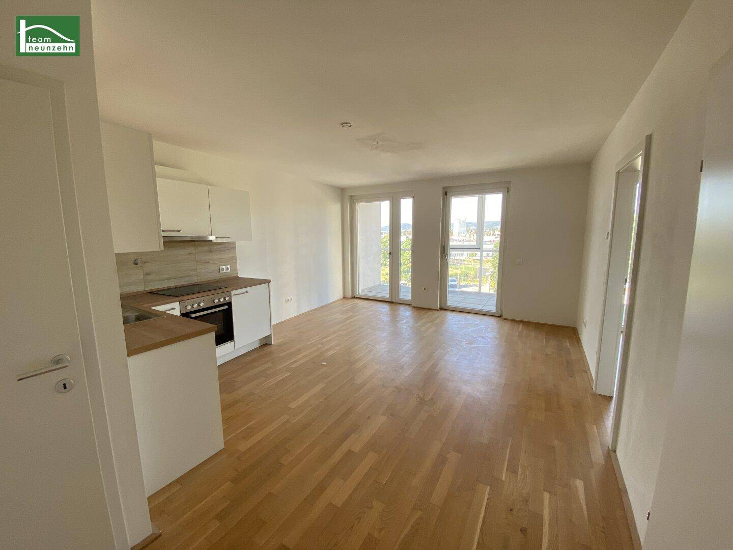 Helles offenes Wohnzimmer mit integrierter Küche, Parkettboden und Zugang zum Balkon.