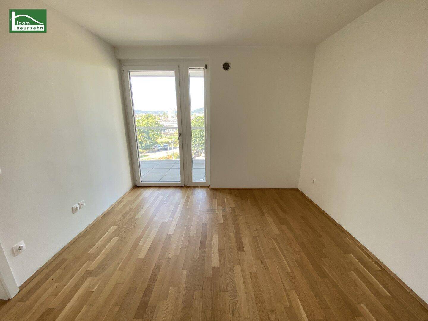 Leeres Schlafzimmer mit Parkettboden und großen Fenstern zum Balkon.