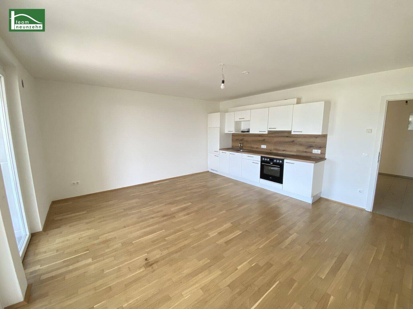 Heller offener Wohnbereich mit integrierter Küchenzeile, Holzboden und viel Tageslicht.