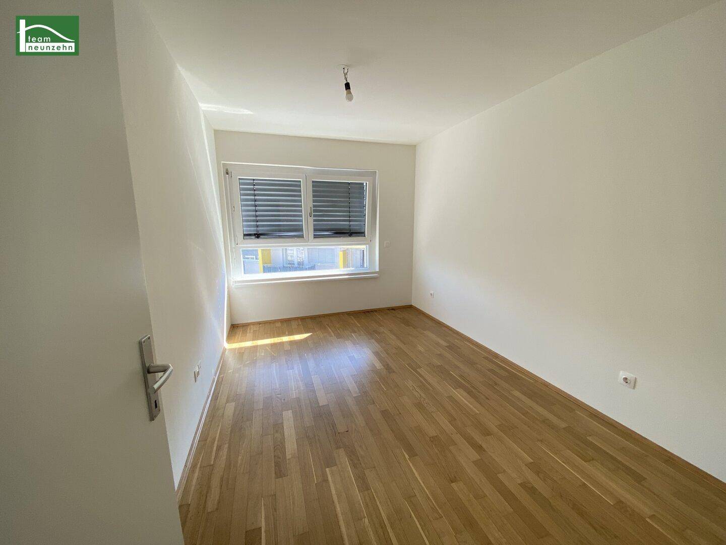 Schlafzimmer mit Holzboden, Fenster und Rollläden für angenehme Verdunkelung.