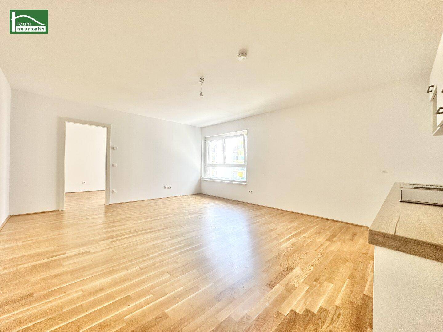 Geräumiger Wohnbereich mit hellem Holzboden und großem Fenster.