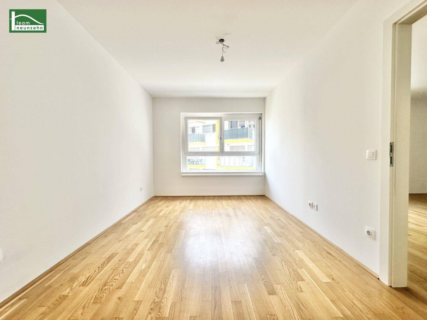 Leeres Schlafzimmer mit Holzboden und Blick auf die umliegenden Gebäude.