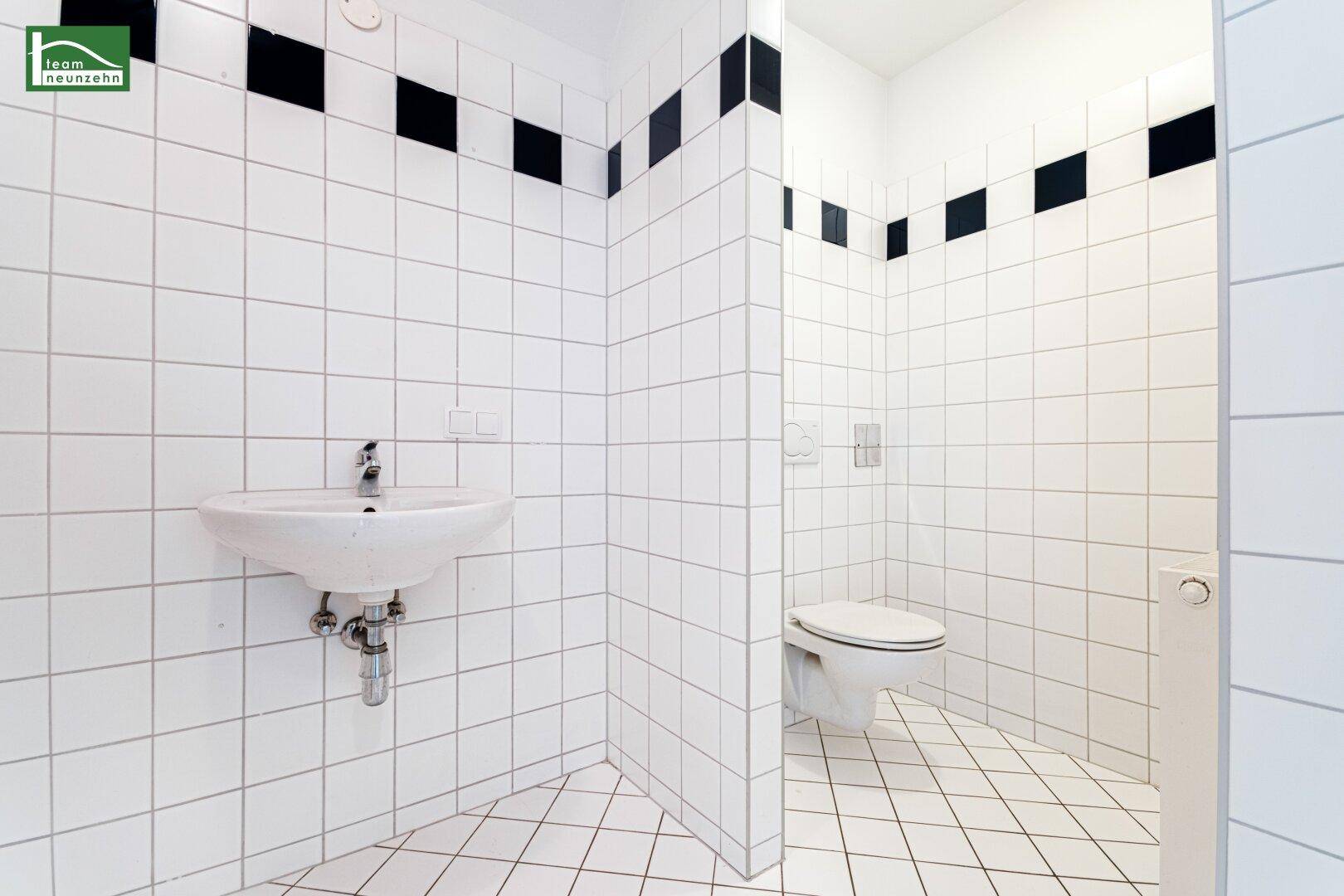 Separate Toilette mit weißen Fliesen, wandhängendem WC und kleinem Handwaschbecken für Gäste.