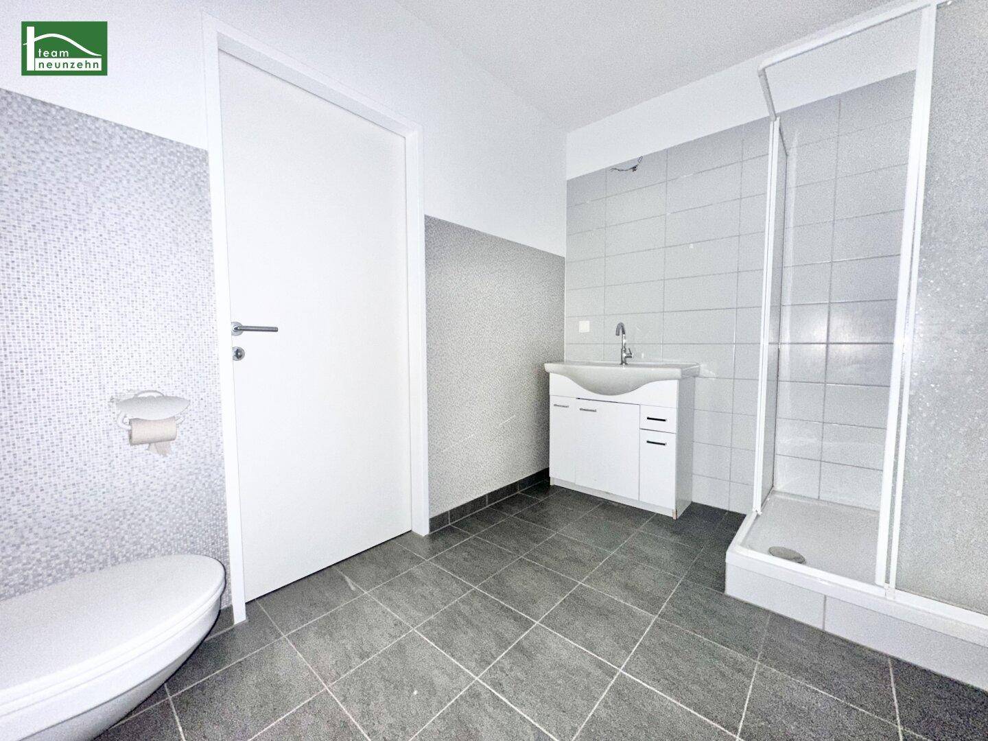 Modernes Badezimmer mit grauen Fliesen, Waschtisch, Toilette und Duschkabine.