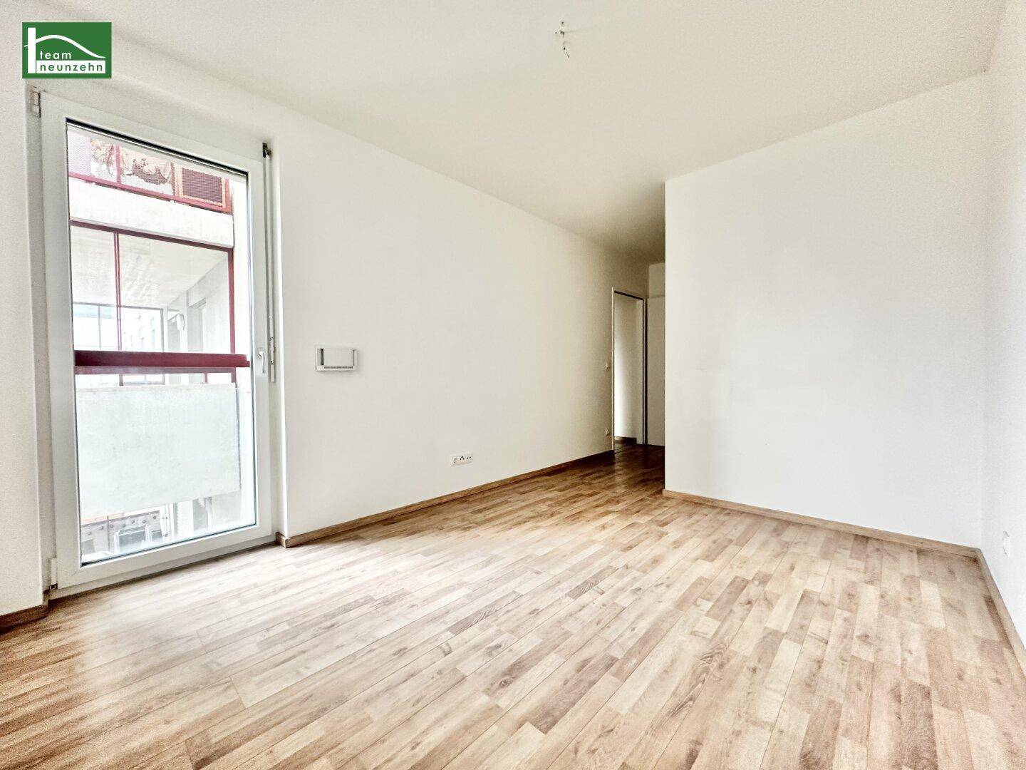 Geräumiges, leeres Zimmer mit Holzboden und Zugang zu einem französischen Balkon.