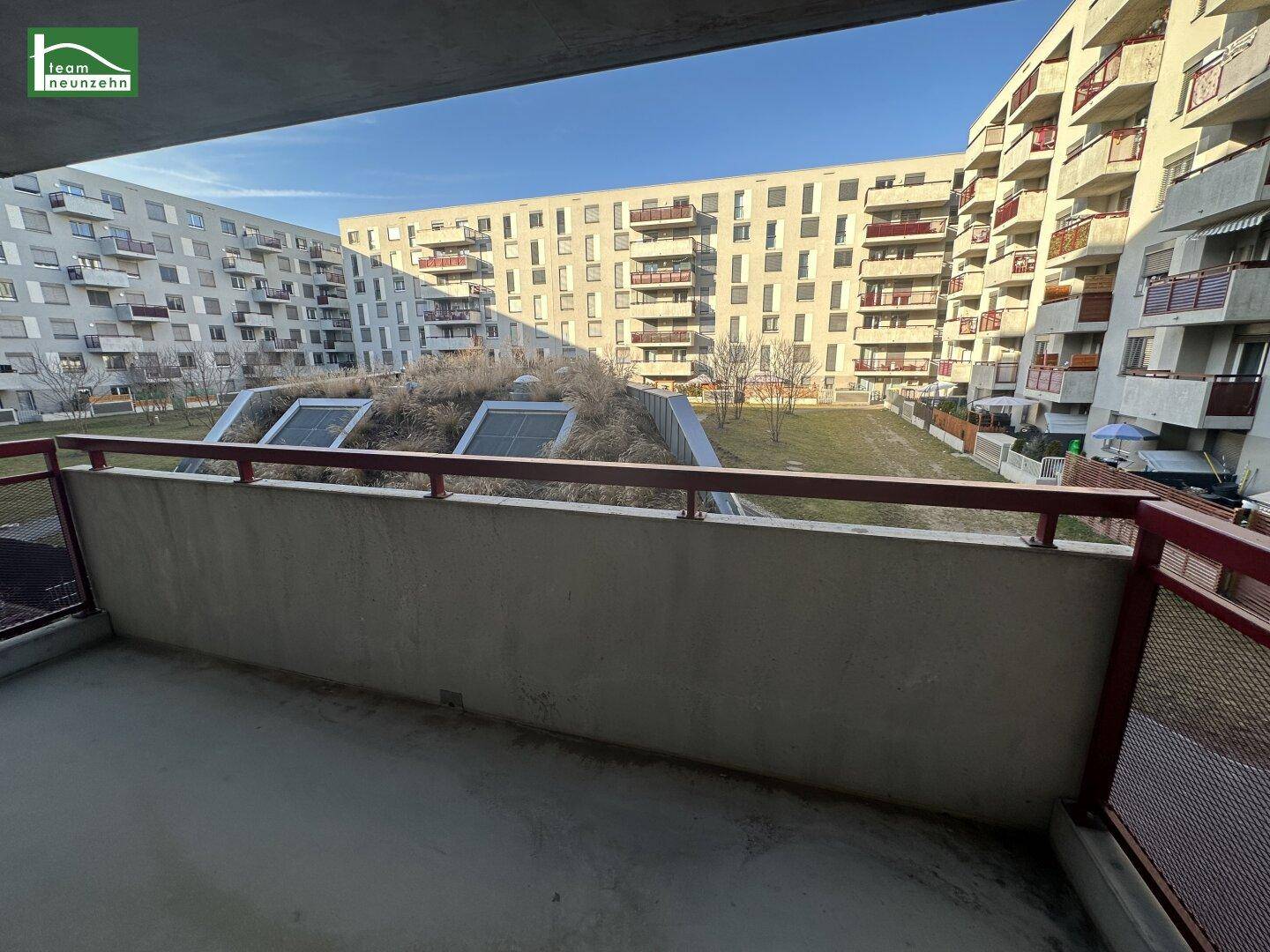 Blick vom Balkon auf den begrünten Innenhof und umliegende Wohngebäude.
