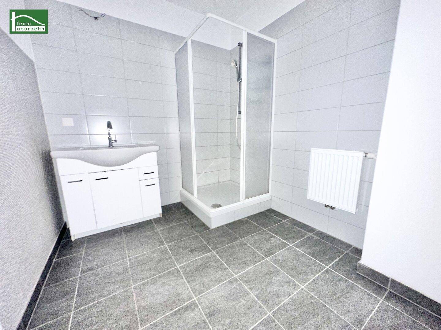 Funktionales Badezimmer mit Duschkabine, Waschbecken und hellen Fliesen.