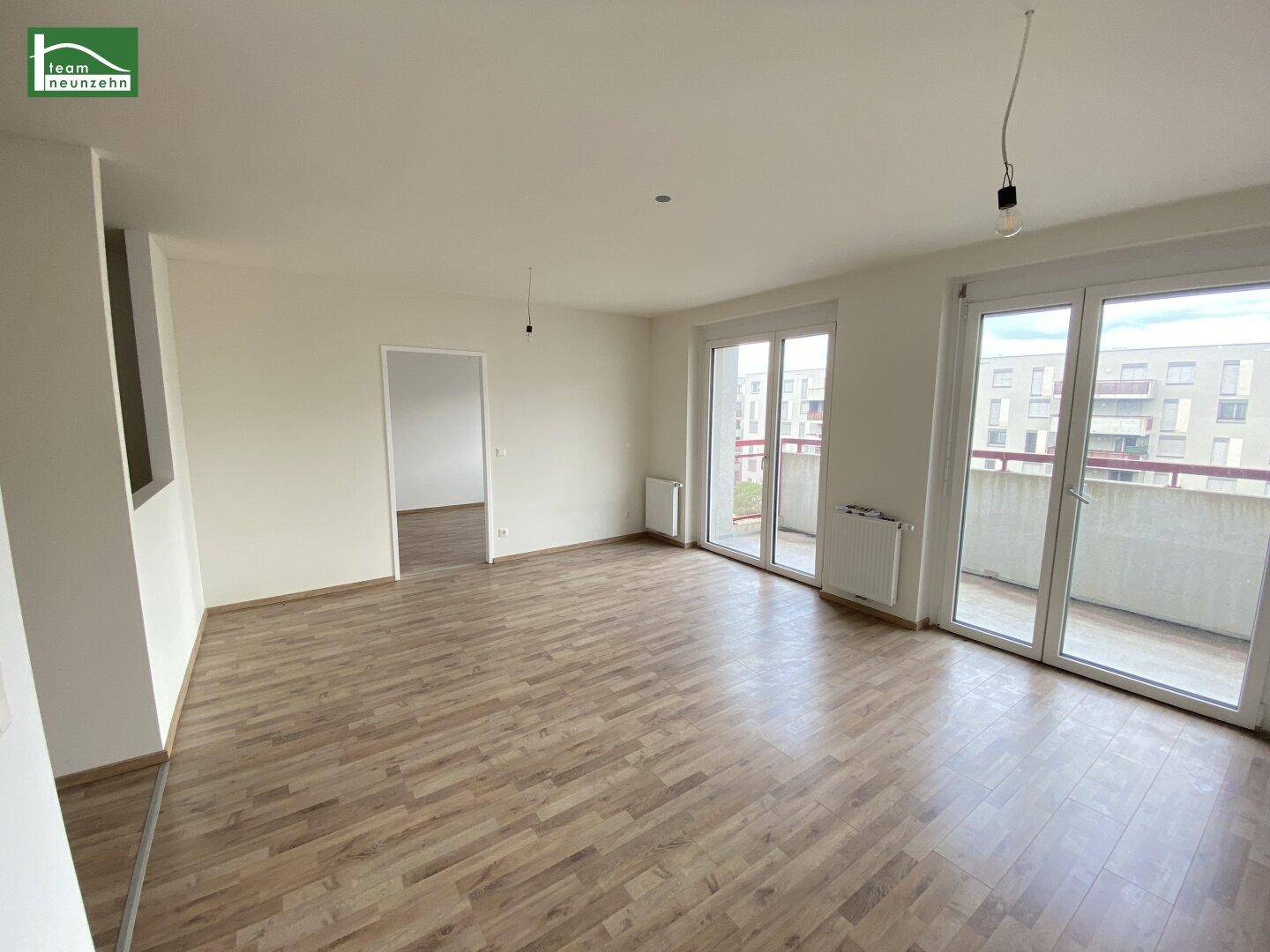 Helles Wohnzimmer mit Laminatboden und Zugang zu einem Balkon, bereit zur individuellen Gestaltung.
