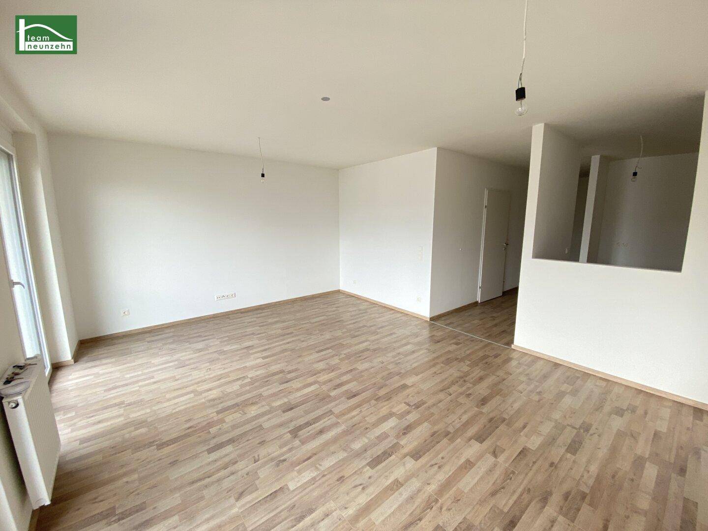 Geräumiger, leerer Wohnbereich mit hellem Laminatboden und weißen Wänden, offen gestaltet.