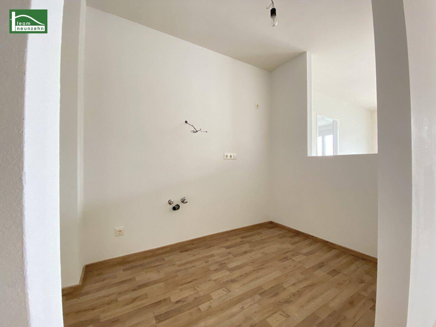 Leerer Küchenbereich mit Anschlüssen für Geräte und hellem Laminatboden, bereit zur Installation.