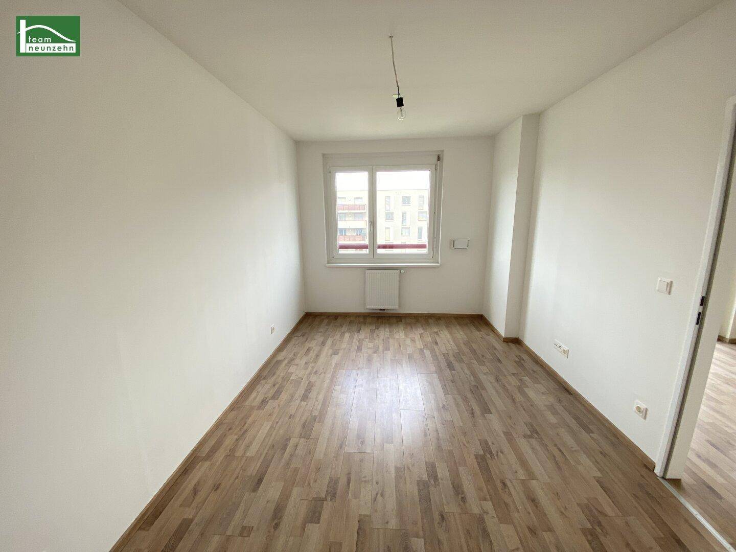 Helles Schlafzimmer mit Laminatboden und einem Fenster, das viel Tageslicht hereinlässt.