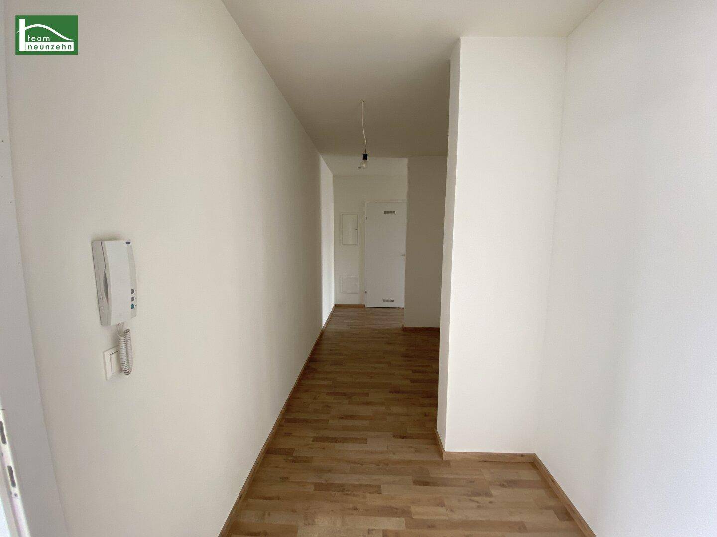 Eingangsbereich mit Laminatboden und Gegensprechanlage, der in den Flur übergeht.