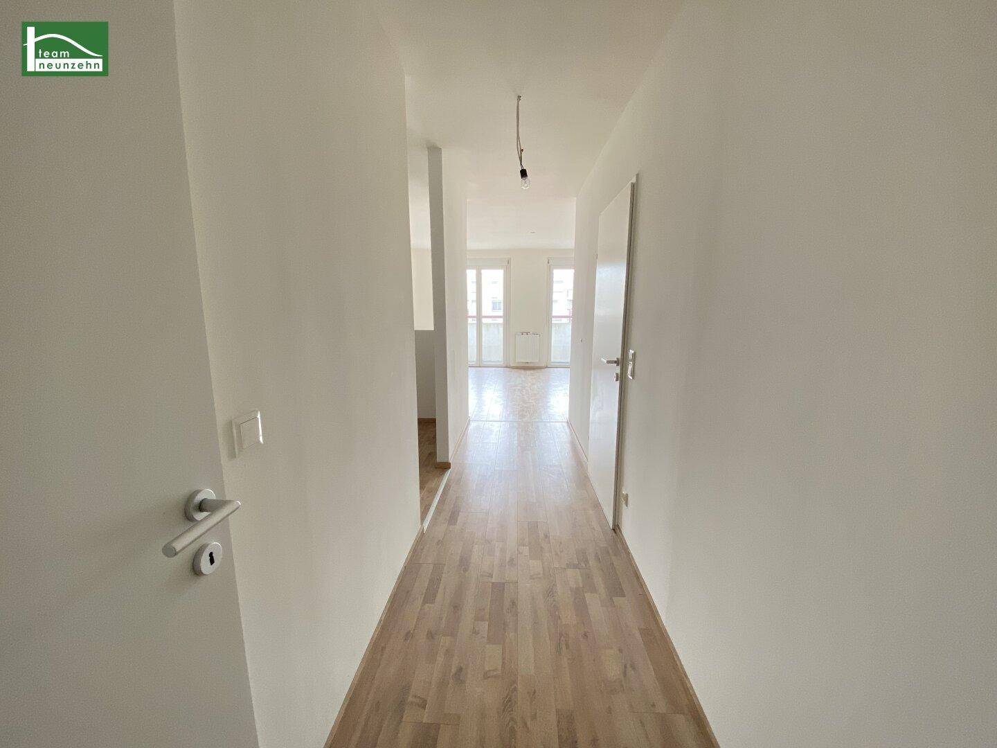 Heller Flur mit Laminatboden und weißen Wänden, der zu den Wohnbereichen führt.