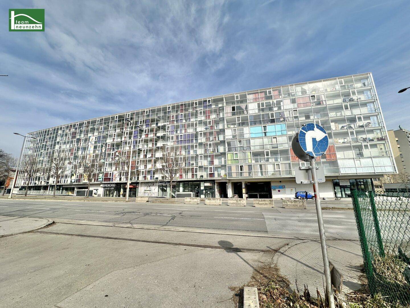Breite Ansicht eines modernen Wohngebäudes mit vielen Fenstern und Geschäften im Erdgeschoss.