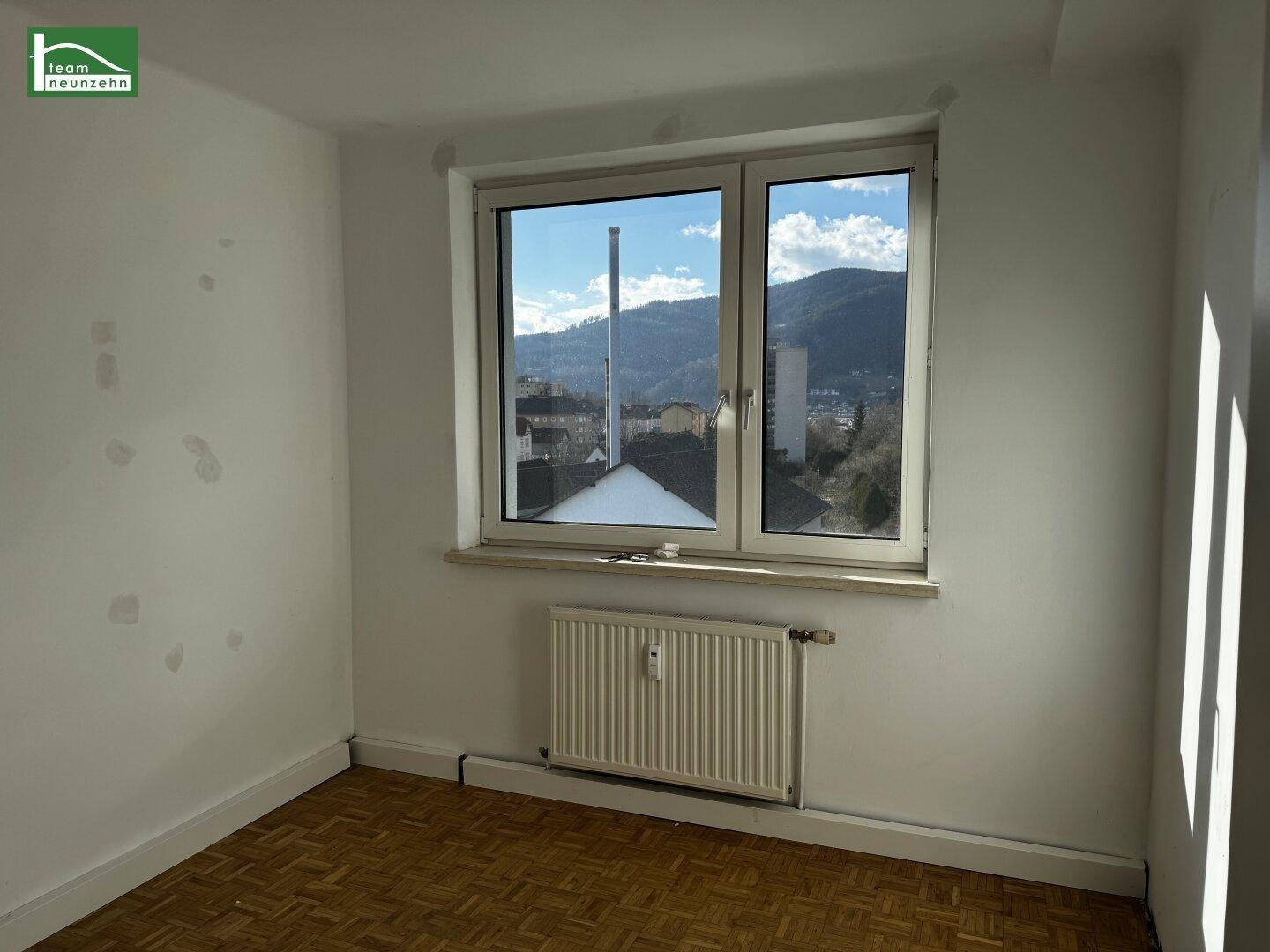 Unmöbliertes Zimmer mit Parkettboden, Heizkörper und Ausblick auf die Berge.