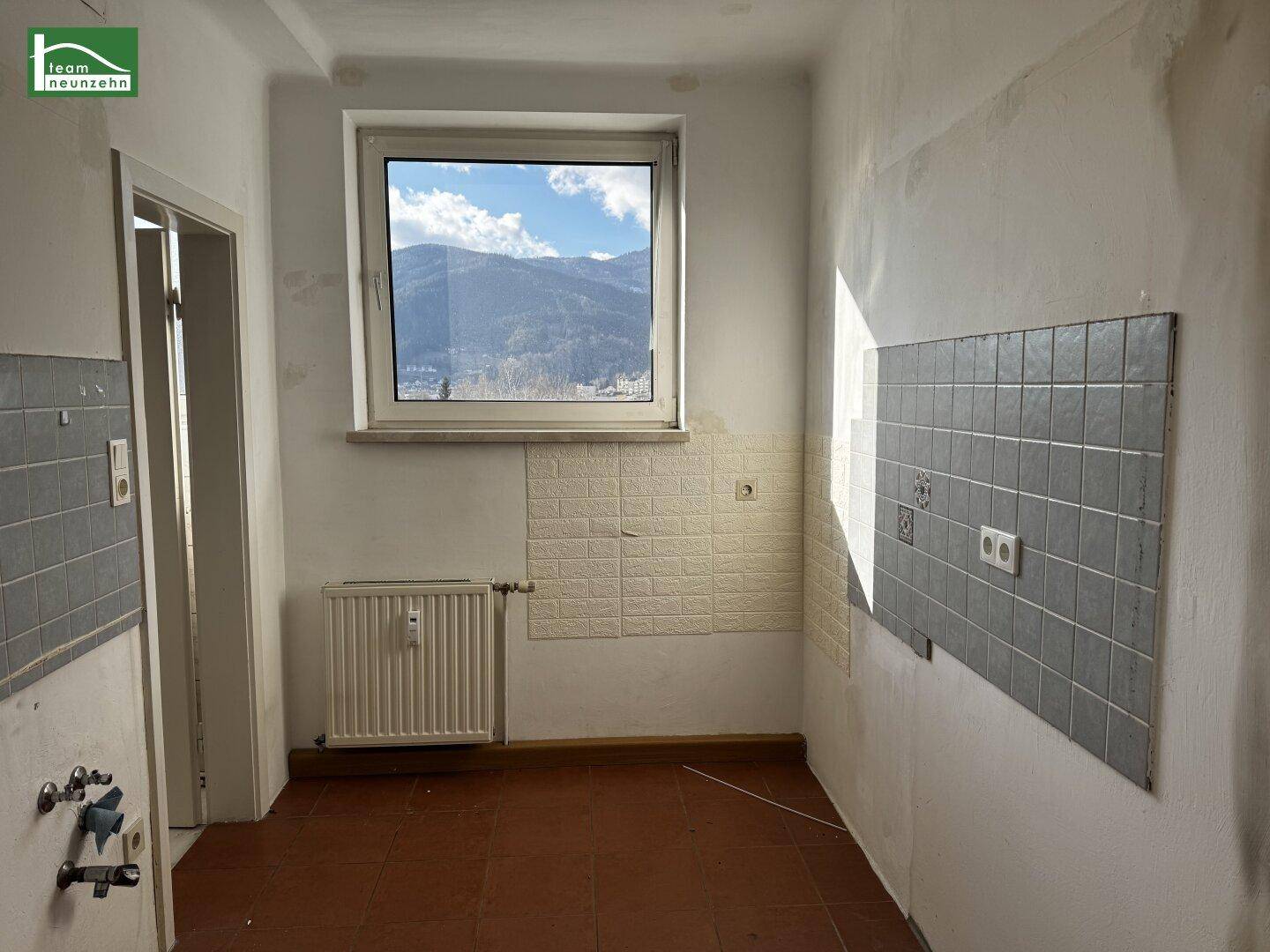 Leere Küche mit Fliesen, Heizkörper und Fenster mit Blick auf die Bergwelt.