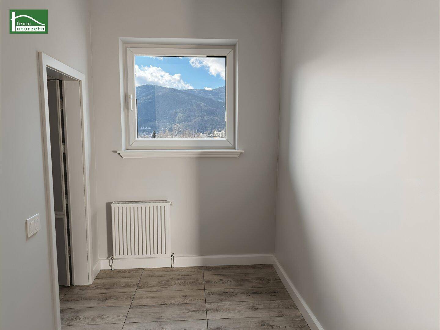 Renovierter Raum mit Fliesenboden, Heizkörper und Fenster mit Bergblick.