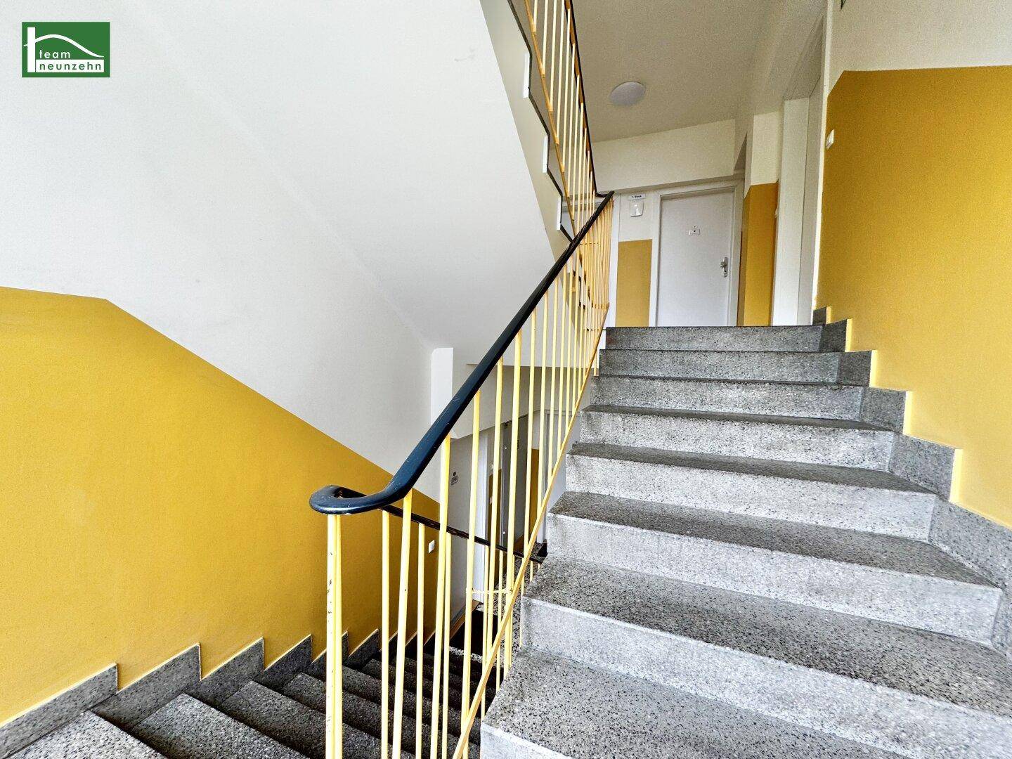 Treppenhaus mit Steinstufen und gelbem Geländer in einem Mehrfamilienhaus.