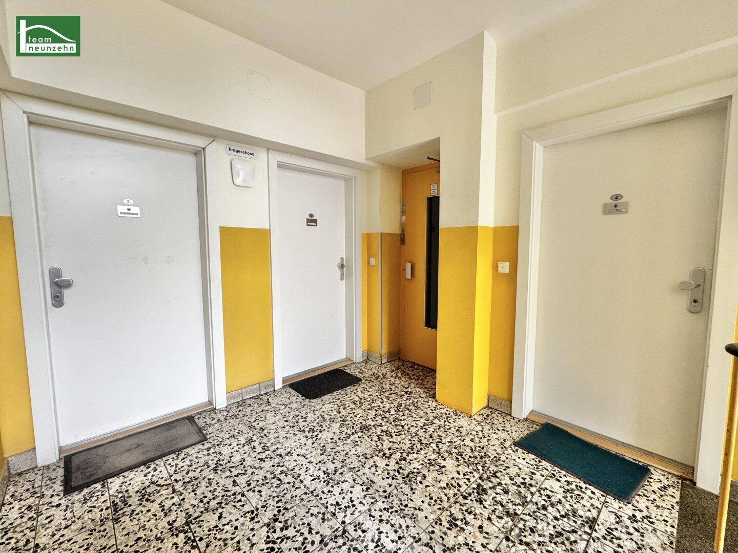 Flur im Eingangsbereich mit mehreren Wohnungstüren, Aufzug und Terrazzoboden.