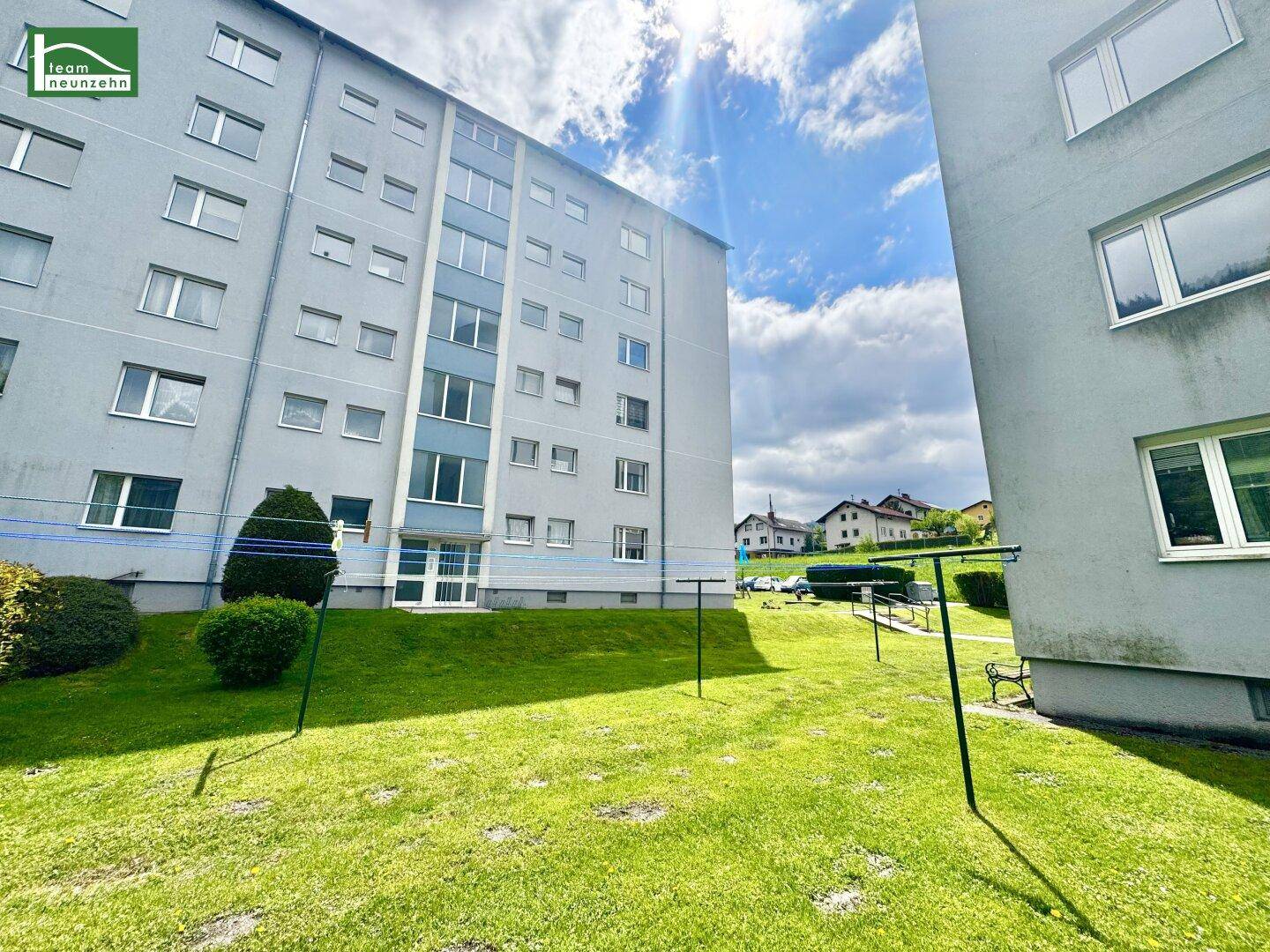 Mehrfamilienhäuser mit großer Rasenfläche und Wäscheleinen im Freien an einem sonnigen Tag.