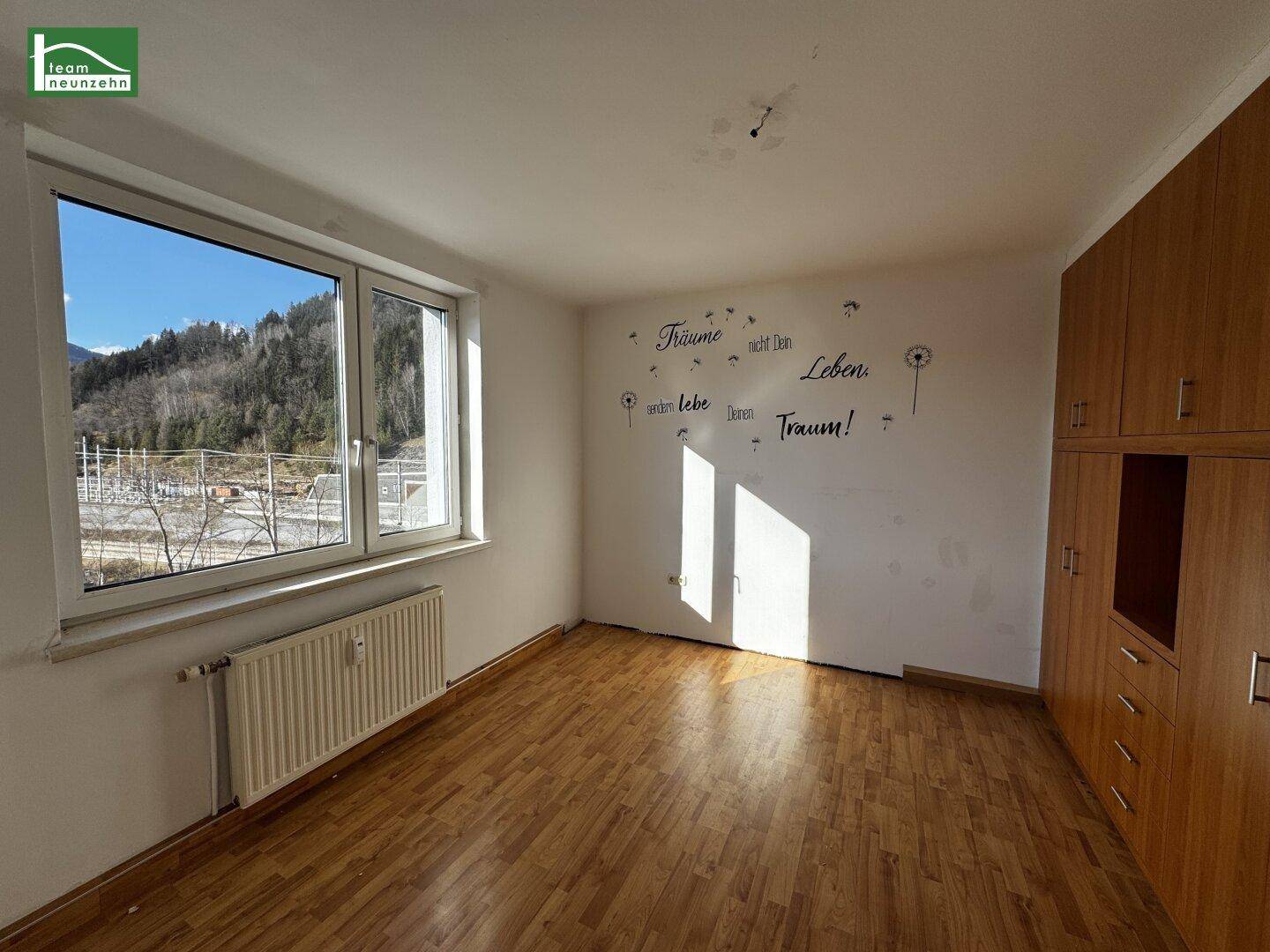 Geräumiges Zimmer mit Holzboden, großem Fenster und Blick auf die grüne Umgebung.