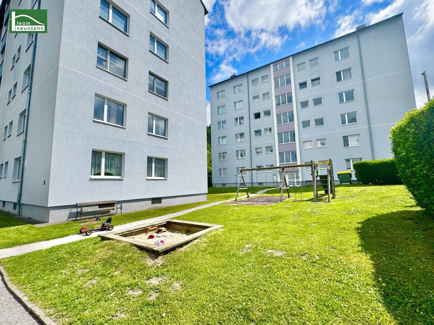 Gemeinschaftsgarten mit Spielplatz und Sandkasten zwischen den Wohngebäuden.