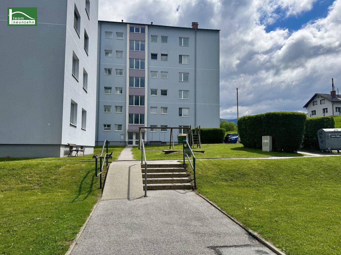 Wohngebäude mit Rampe und Treppe zum Eingang, umgeben von Grünflächen.