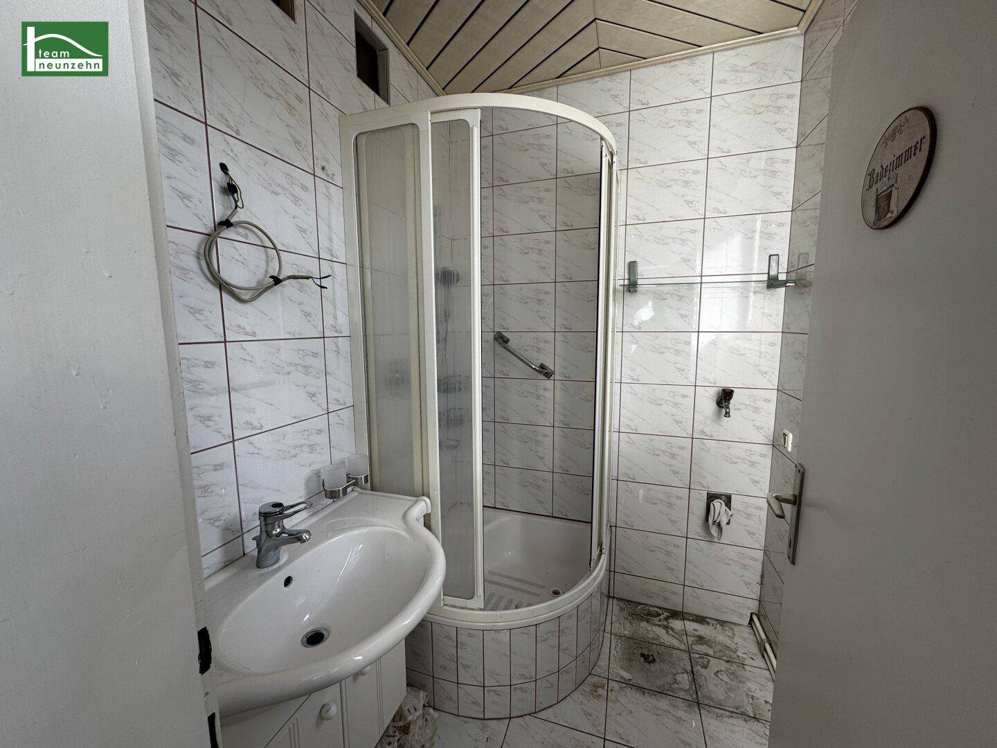 Badezimmer mit Duschkabine, Waschbecken und weißen Fliesen an Wänden und Boden.