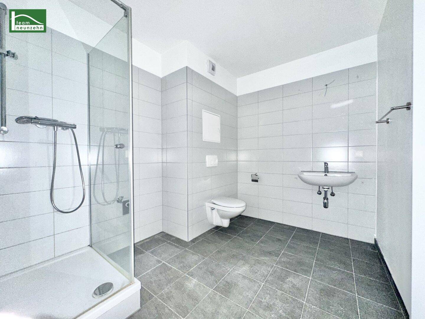 Modernes Badezimmer mit grauen Fliesen, Duschkabine, wandhängendem WC und Waschbecken.