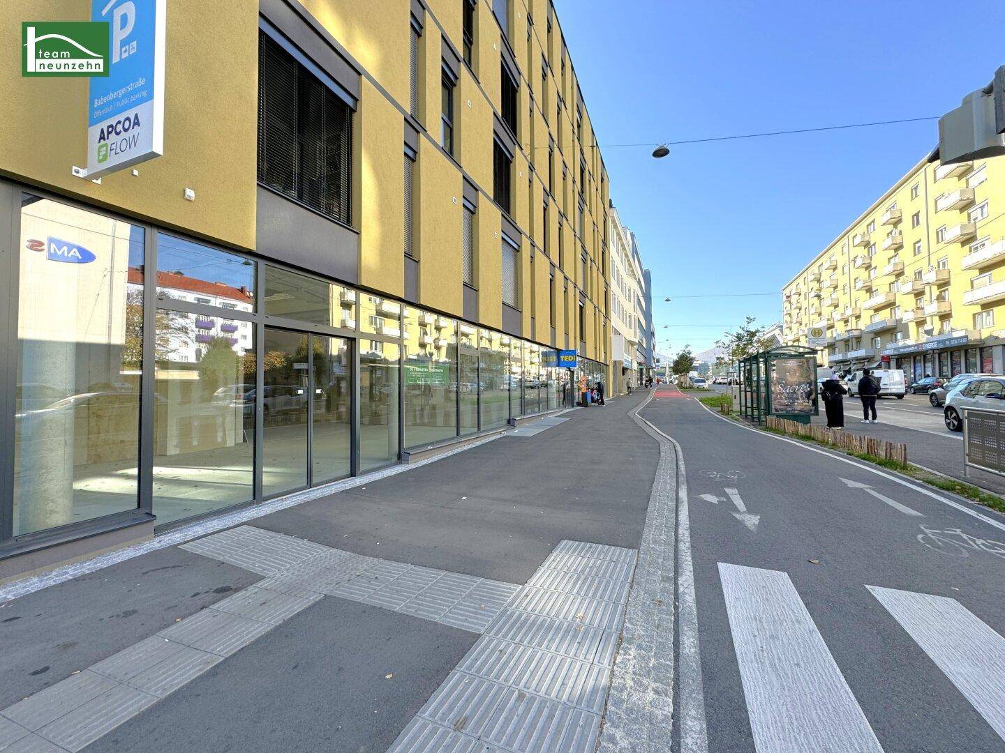 Straßenansicht des modernen Gebäudes mit breitem Gehweg und großen Schaufenstern.