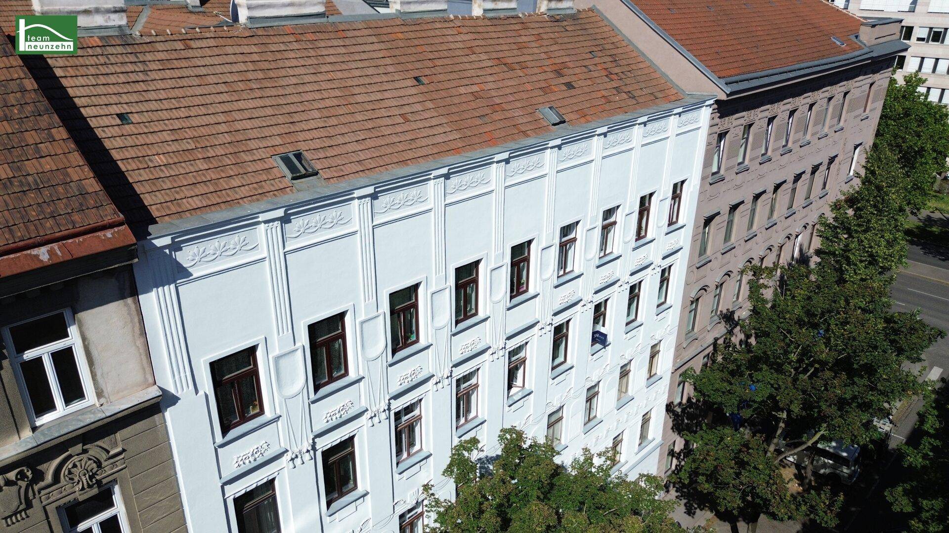 Schrägansicht des Altbaus von oben mit rotem Dach, Dachfenstern und angrenzenden Gebäuden.