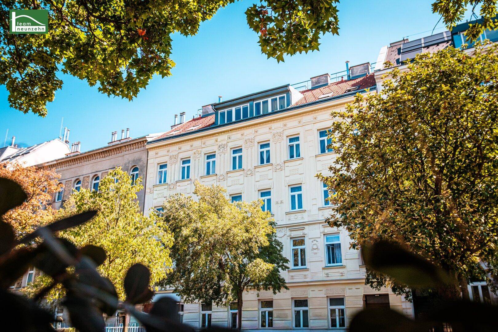 Historische Fassade eines renovierten Gebäudes mit modernen Dachausbauten und grüner Umgebung.