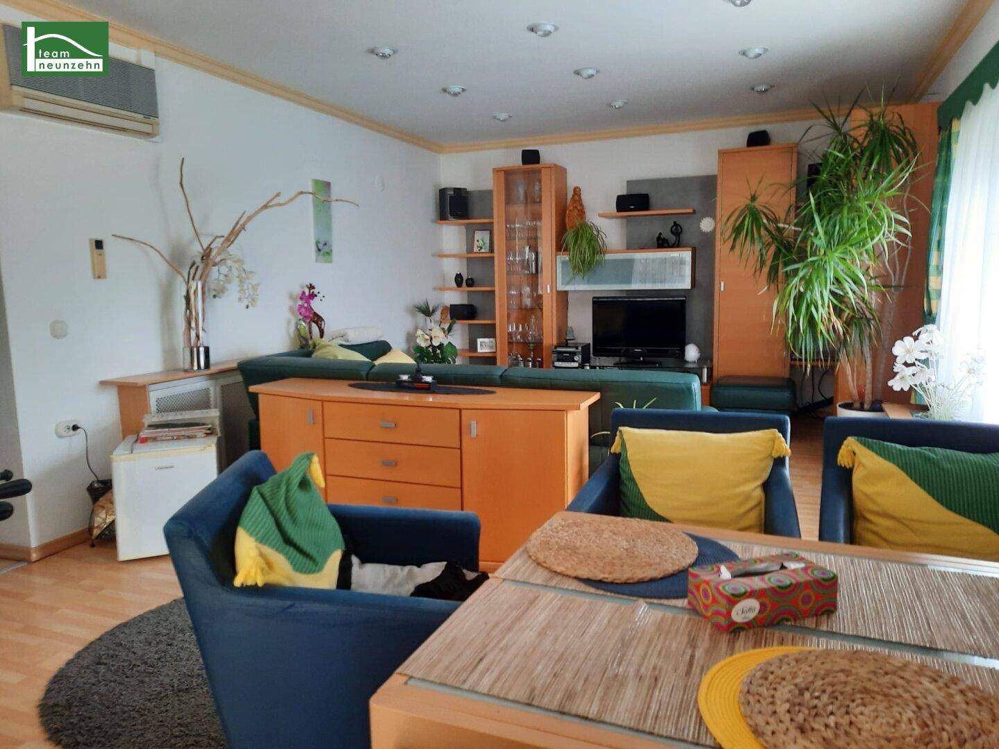 Gemütliches Wohnzimmer mit Holzboden, vielen Pflanzen und einer bequemen Sitzecke.