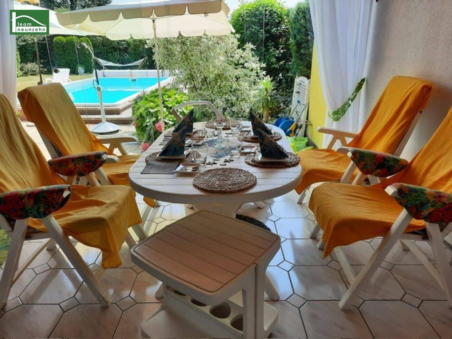 Überdachte Terrasse mit Esstisch und Stühlen, Blick auf den Poolbereich im Garten.