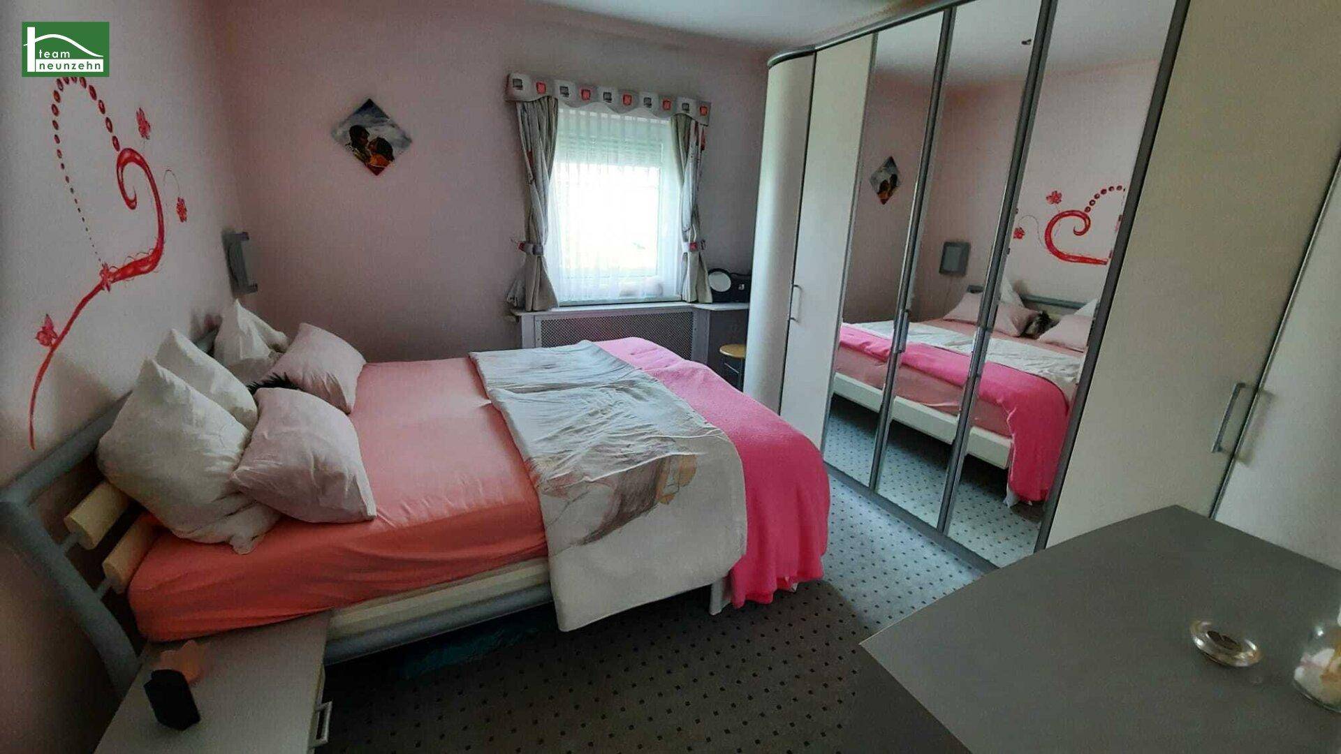 Schlafzimmer mit rosa Wänden, Doppelbett und Spiegelschränken, dekoriert mit Herzmotiven.