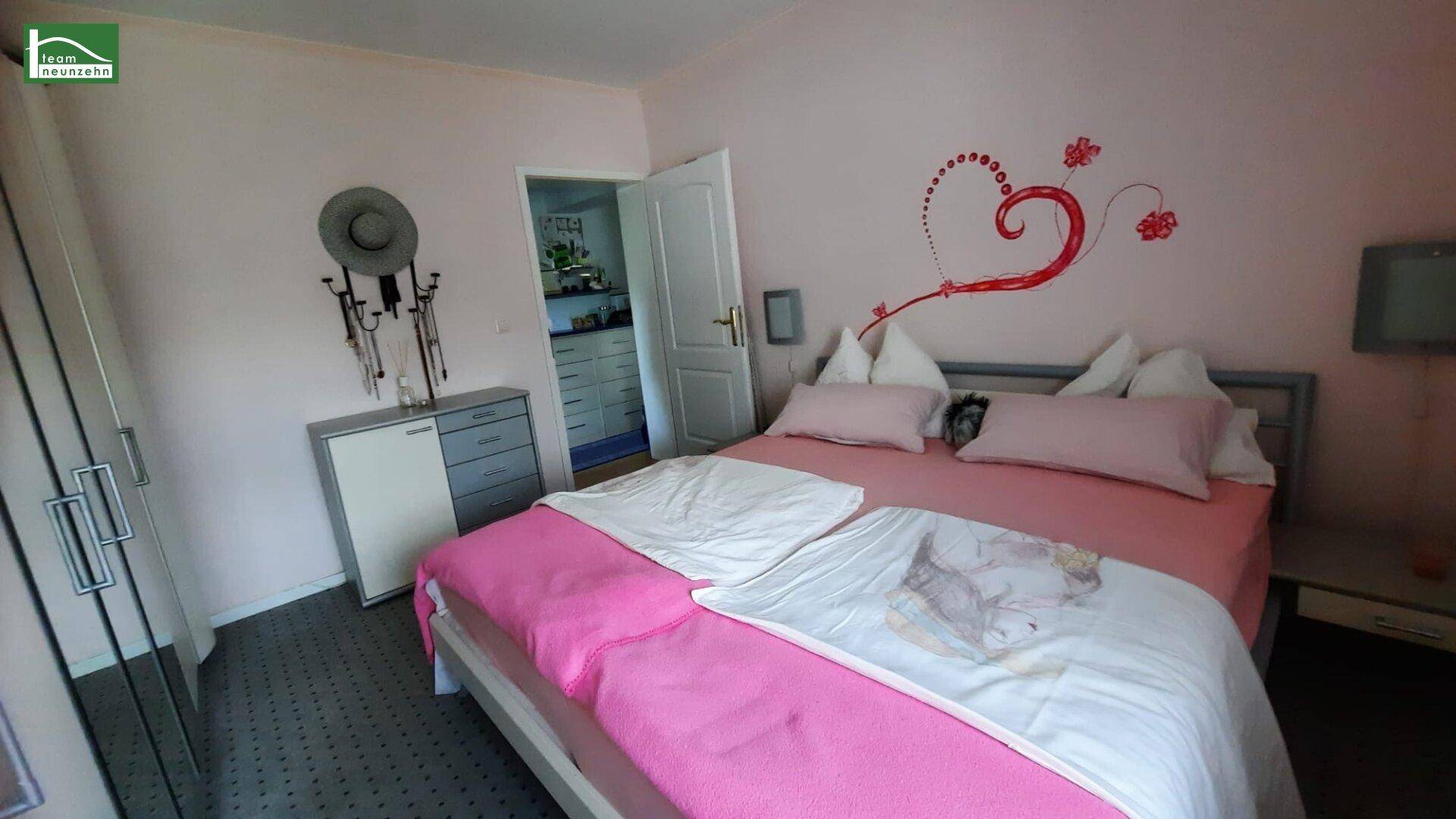Schlafzimmer mit rosa Wänden, Doppelbett und Zugang zu einem weiteren Raum.