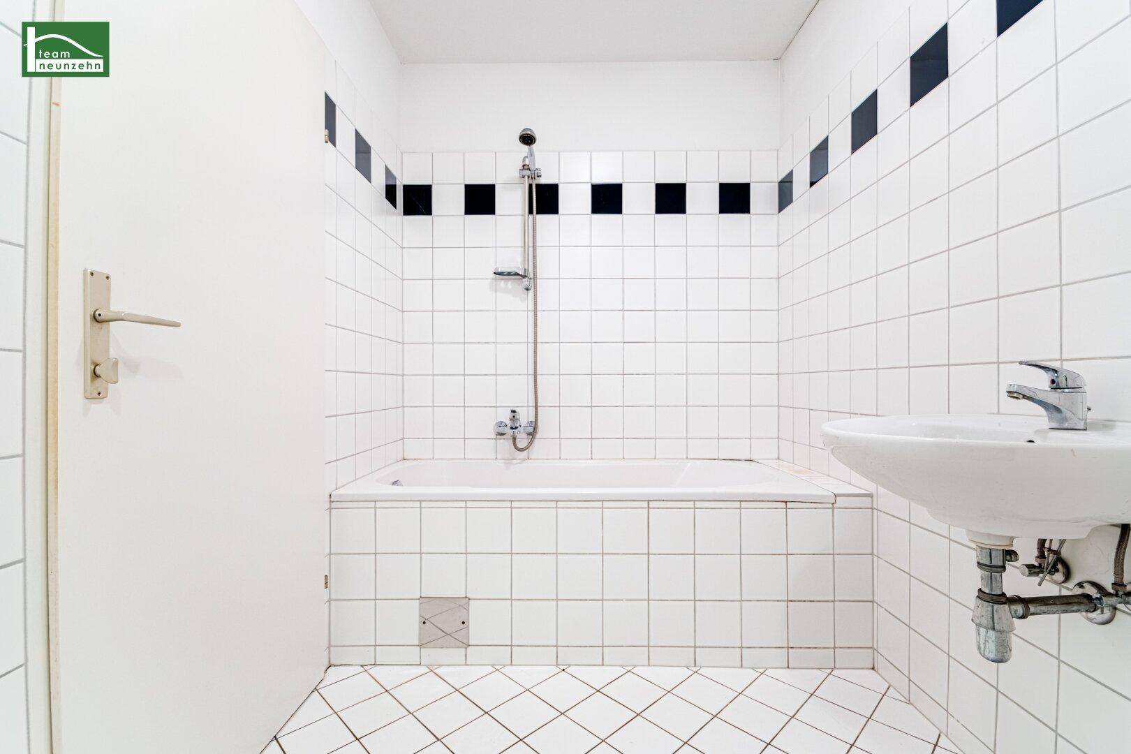 Badezimmer mit Badewanne, Duschfunktion und Waschbecken, gefliest in Weiß mit schwarzem Akzent.