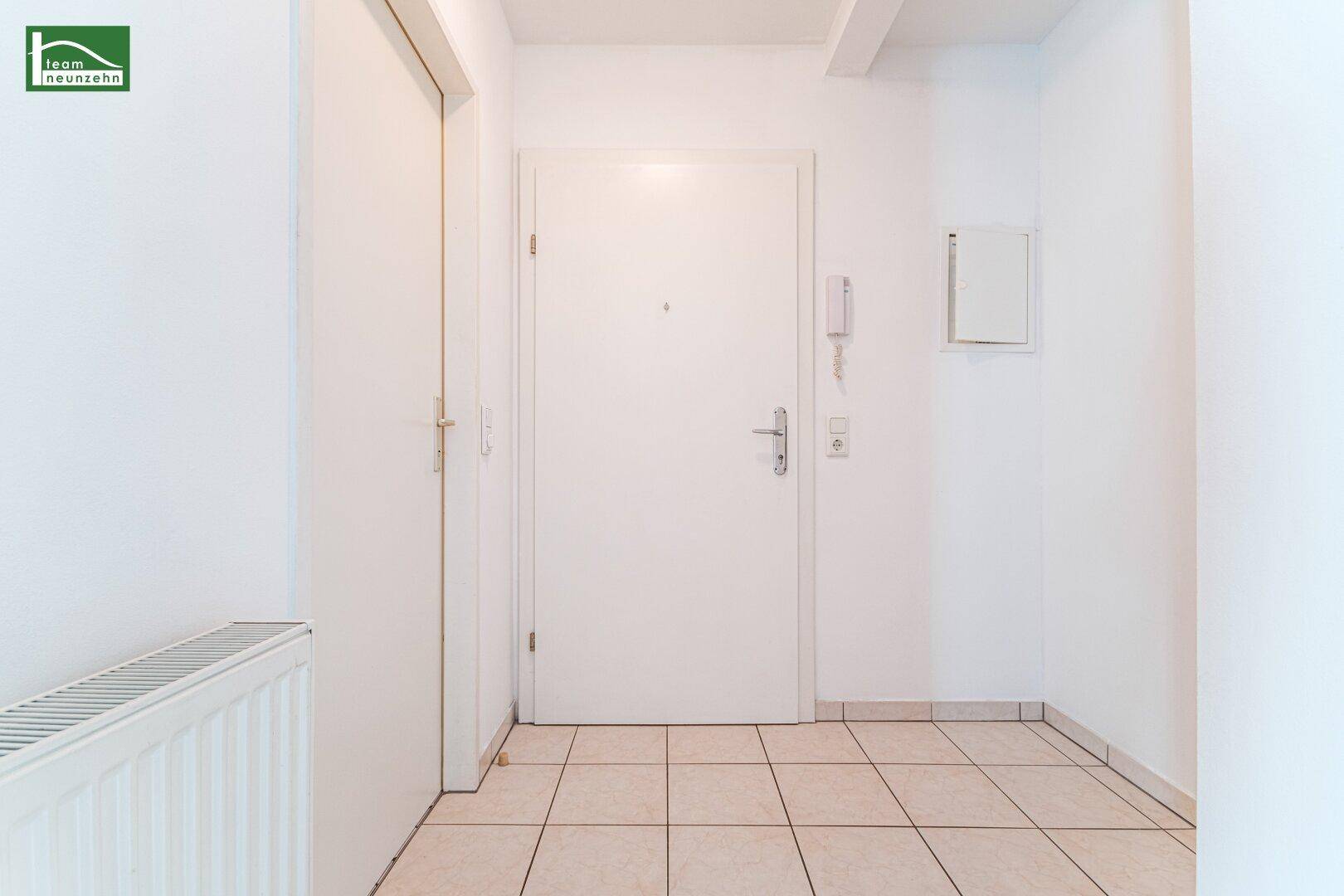 Heller Eingangsbereich mit Fliesenboden, Gegensprechanlage und weißer Wohnungstür.