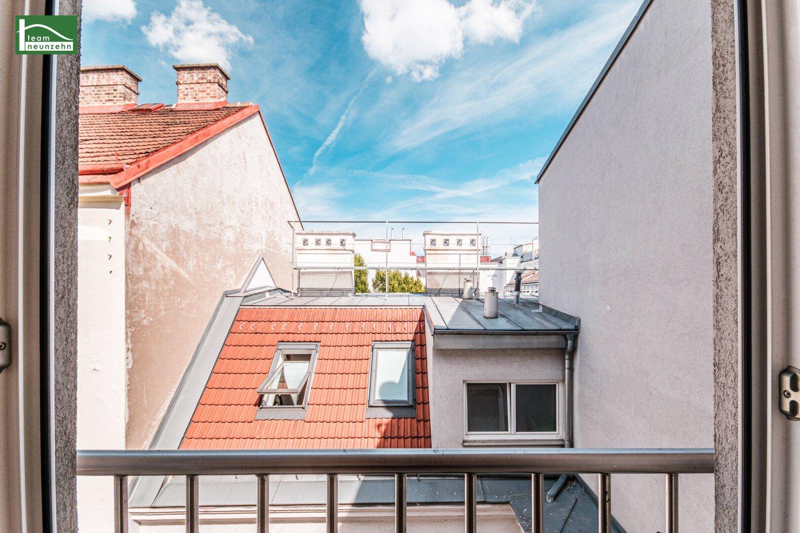 Ausblick von einem Balkon auf umliegende Dächer und den blauen Himmel.