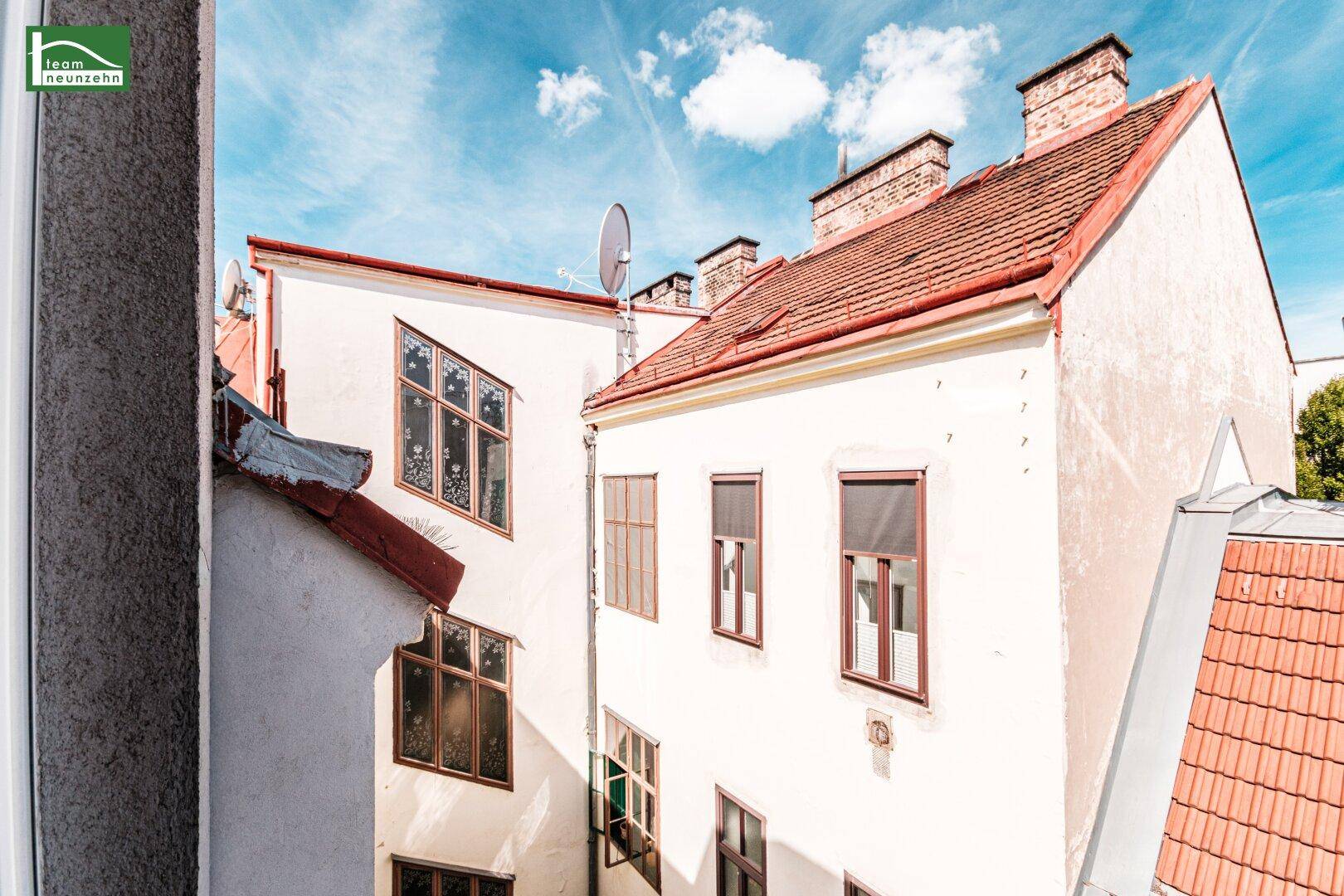 Blick aus dem Fenster auf die Rückseite historischer Gebäude und Dächer im Innenhof.