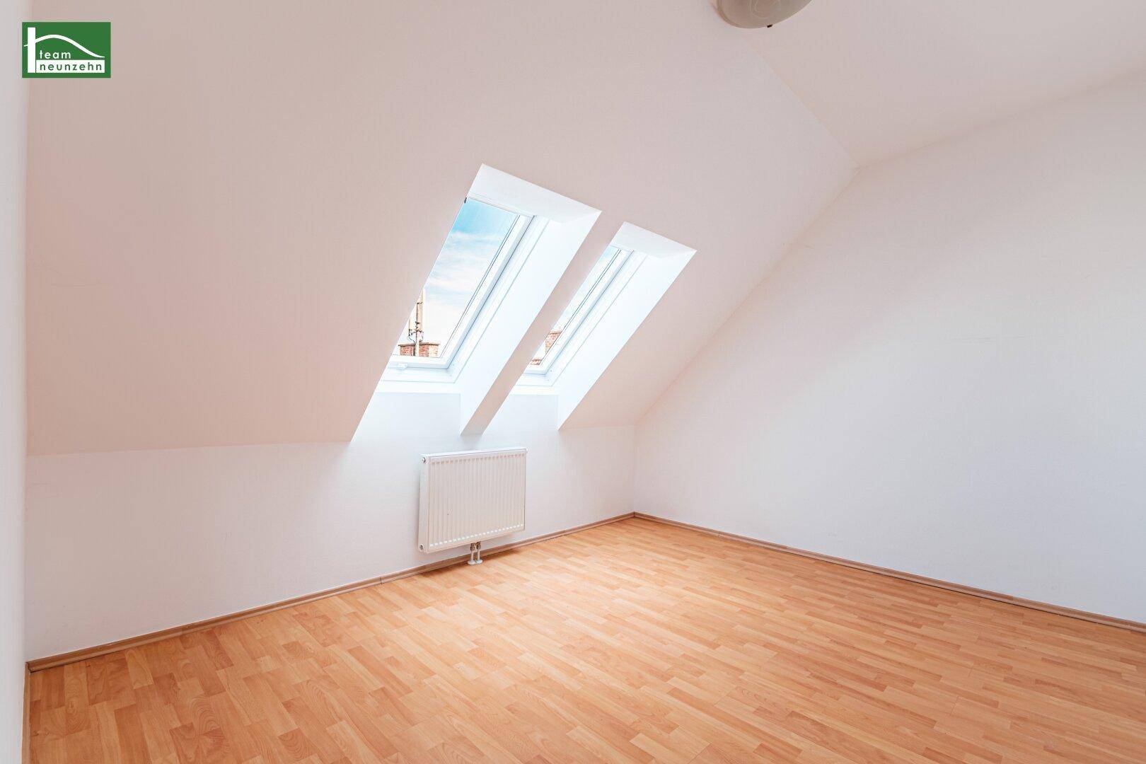 Heller, leerer Raum im Dachgeschoss mit Holzboden, Dachschräge und zwei Dachfenstern.