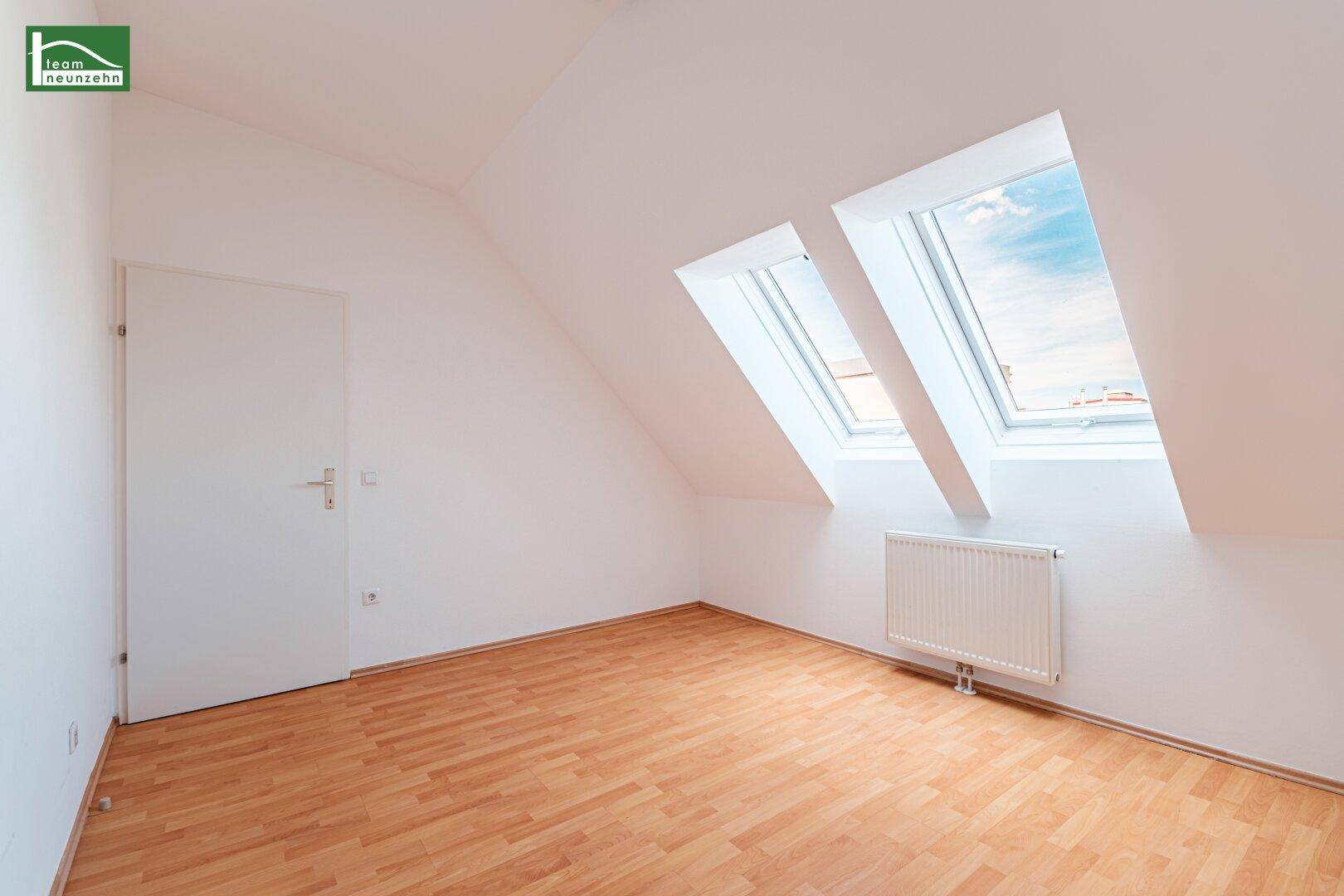 Heller, leerer Raum im Dachgeschoss mit Holzboden, Dachschräge und zwei Dachfenstern.