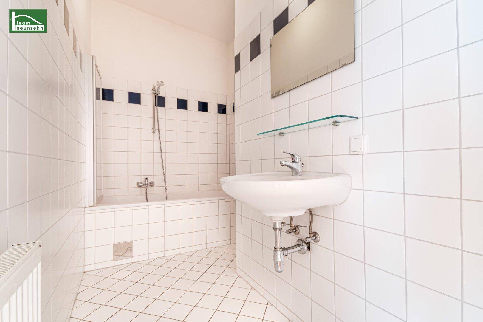 Gefliestes Badezimmer mit Badewanne, Waschbecken und einem klassischen weiß-schwarzen Fliesenmuster.
