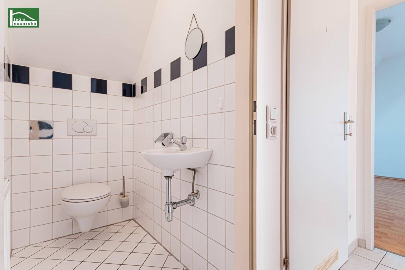 Kleines Gäste-WC mit Fliesenboden, Waschbecken und wandmontierter Toilette.
