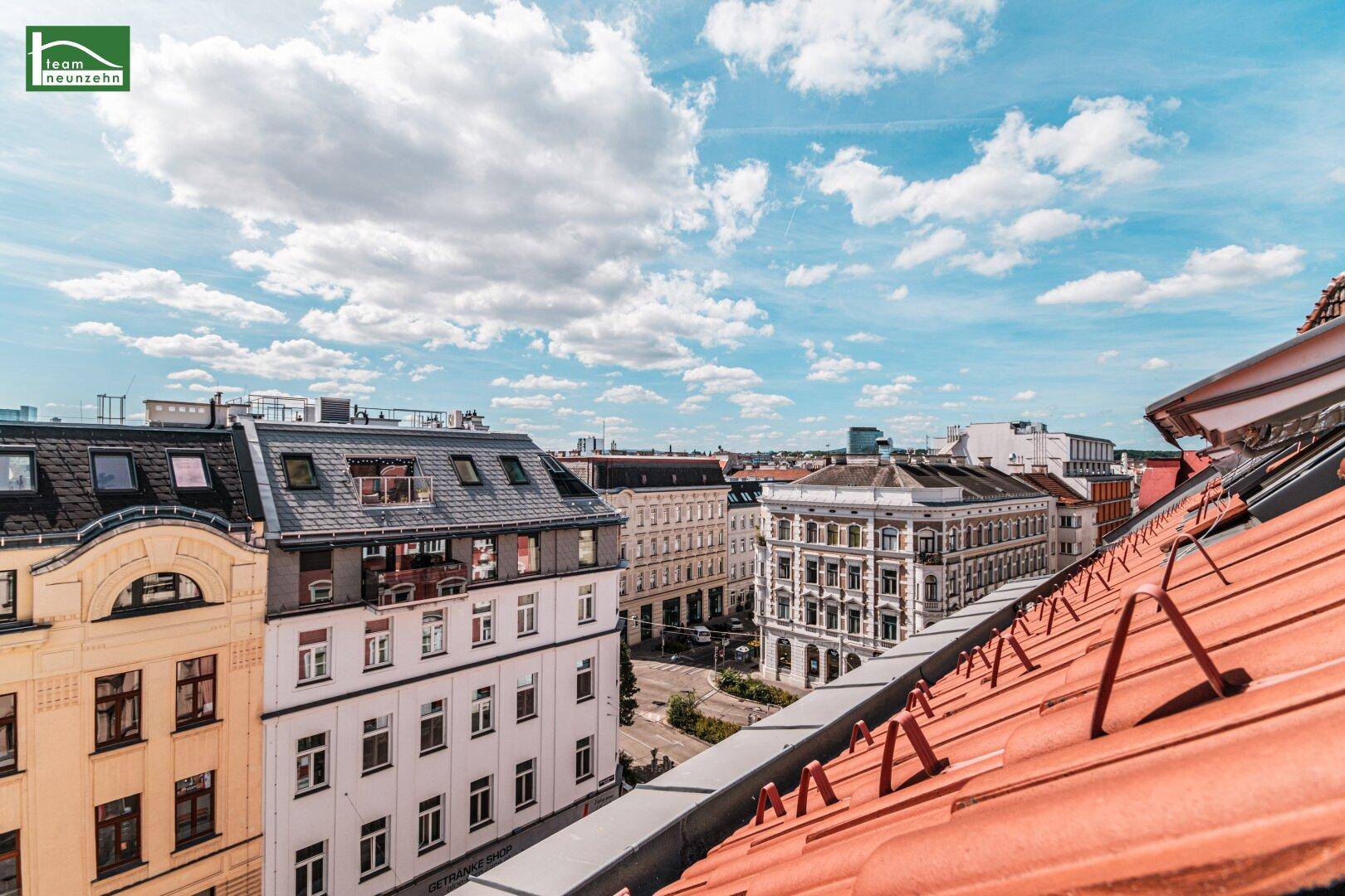 Weiter Stadtblick über die Dächer und historische Gebäude unter einem strahlend blauen Himmel.