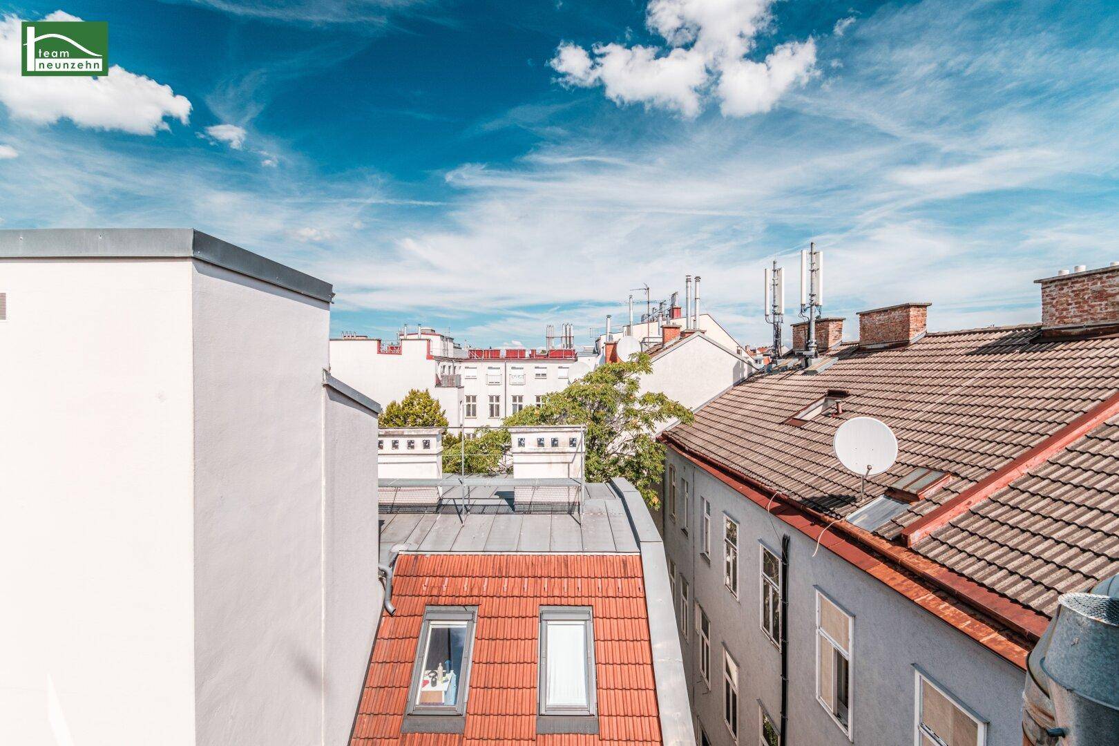 Blick über die Dächer der Stadt mit Antennen und Wohngebäuden unter blauem Himmel.